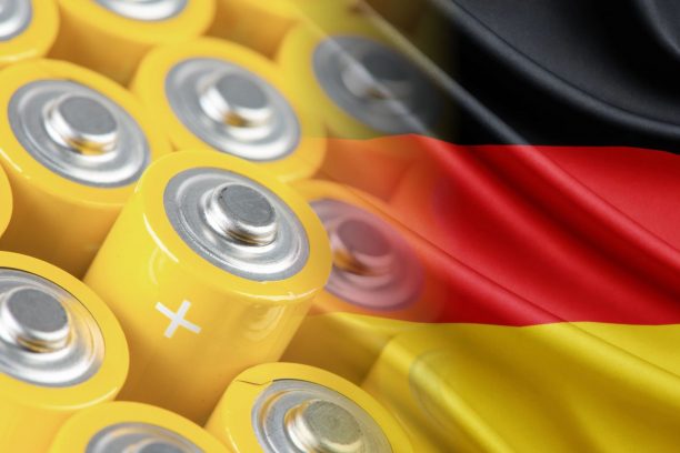 Close-up of yellow cylindrical batteries with visible positive terminals, overlaid by a waving German flag
