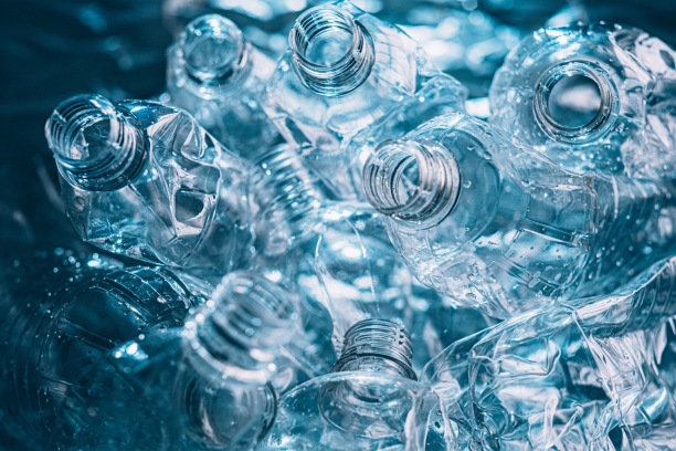 Close-up of several crushed clear plastic water bottles with visible necks and water droplets illuminated by cool blue light.