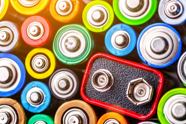 Colorful assortment of cylindrical batteries clustered around a red-edged 9V battery, shown from the positive terminals.
