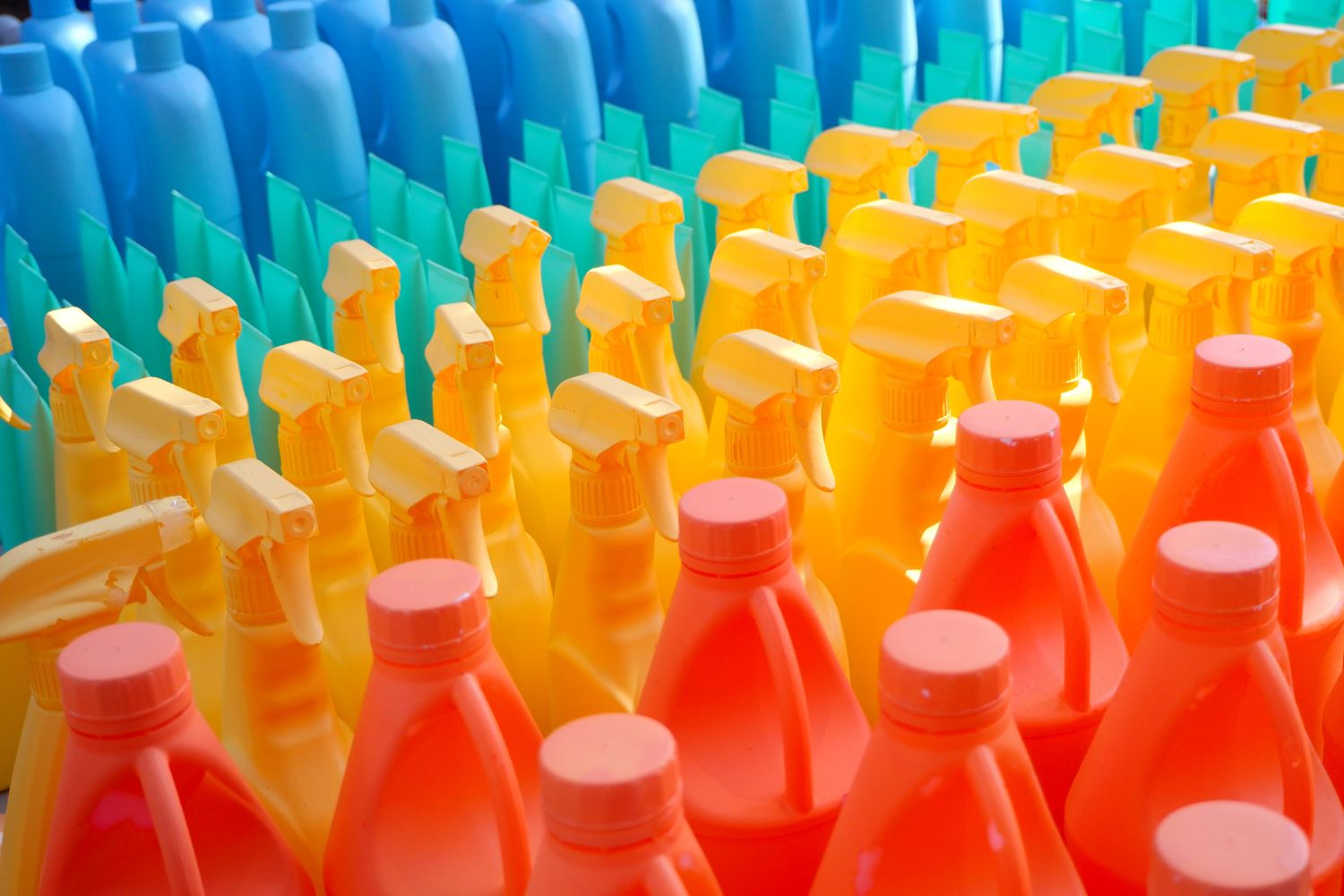 Rows of colorful plastic spray bottles arranged in a gradient from blue to yellow to red.