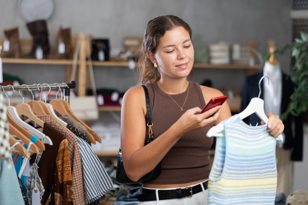 Woman scans the QR code of the topic on mobile phone with interest and reads the detailed composition on the manufacturer's website. Woman with phone in hands in clothing store